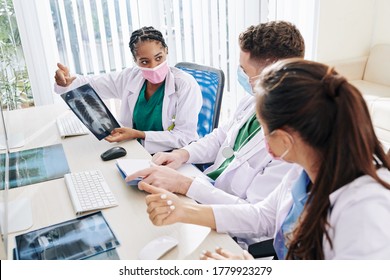 Serious Young Black Female Doctor In Medical Mask Showing Lungs X-ray Of Patient With Suspected Coronavirus To Colleagues