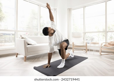 Serious young Black man doing morning exercises at home, keeping twisting yoga asana on mat, caring for wellness, fit, wellbeing, healthy active lifestyle, training body in apartment - Powered by Shutterstock