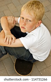 Serious young boy sitting on a skateboard with his arms crossed