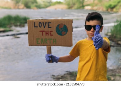 A Serious Young Boy Wearing A Yellow T-shirt And Blue Gloves Holding A Cardboard Sign Drawn By Hand With The Symbol Of A Terrestrial Globe And On Which He Puts An Ecological Message With Thumb Up.