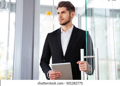 Serious Young Businesman Holding Tablet And Entering The Door In Office