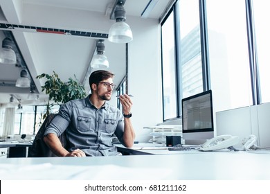 Serious young businessman sitting and talking on mobile phone in office. Creative professional sitting at his workplace. - Shutterstock ID 681211162