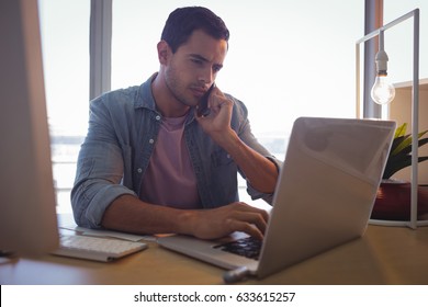 Serious Young Businessman Talking On Phone While Working At Creative Office