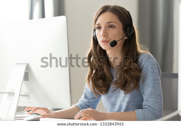 Serious young businesswoman in wireless headset\
call center agent telemarketer consulting client participating\
business video conference talk help as customer care service\
support helpline in\
office