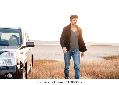 Serious Young Casual Man Walking Near His Car At The Seaside