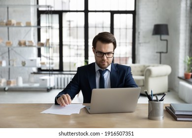 Serious young Caucasian male boss or CEO sit at desk in office work online on laptop consulting clients on web. Focused businessman look at computer screen watch webinar make notes on paperwork. - Powered by Shutterstock