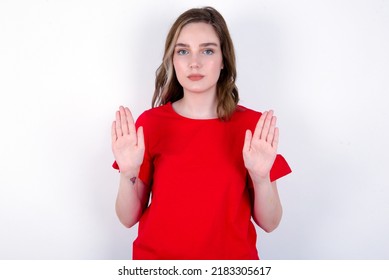 Serious Young Caucasian Woman Wearing Red T-shirt Over White Background Pulls Palms Towards Camera, Makes Stop Gesture, Asks To Control Your Emotions And Not Be Nervous