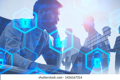 Serious young computer engineer working on laptop over abstract city background with business people with double exposure of online security interface. Toned image