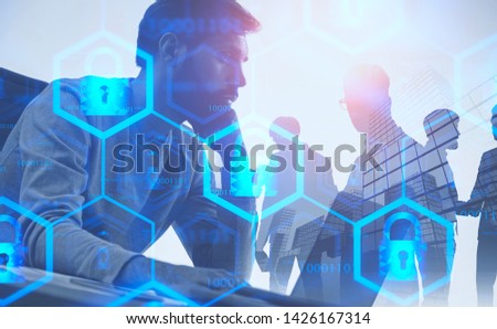 Serious young computer engineer working on laptop over abstract city background with business people with double exposure of online security interface. Toned image