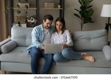 Serious Young Couple Sit On Sofa By Laptop Consider On Making Expensive Purchase Discuss Wedding Planning. Loving Millennial Spouses Surf Internet Together Search For New House Apartment To Buy Rent