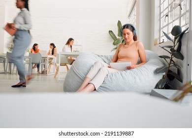 Serious, Young Design Student Relaxing And Reading Or Listening To Music In Break Room In Startup Office, With Colleagues. Modern Creative Designer Working On Tablet In Casual Informal Business