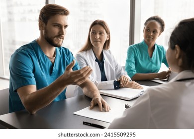 Serious young doctor man speaking to diverse colleagues, discussing job, medical profession, giving surgeon expertise, consultation for difficult patient case. Clinic staff talking at meeting table - Powered by Shutterstock