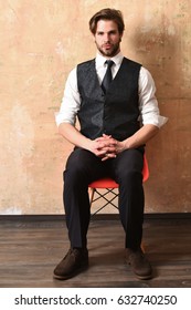 Serious Young Fashion Business Man In Classy Suit And Tie Sitting Straight On Chair On Beige Background