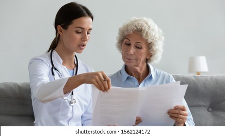 Serious young female doctor nurse explain medical health insurance contract form hold papers talk to elder old grandma patient read service agreement discuss test result during homecare visit concept