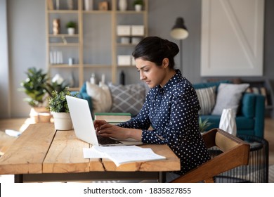 Sério jovem focado 30 anos mulher de negócios indiana estudante freelancer sentar na mesa em um escritório doméstico moderno aconchegante sala de estar enviando mensagens de texto no laptop, fazer trabalho remoto remotamente, resolvendo problemas de forma distante conceito Foto Stock
