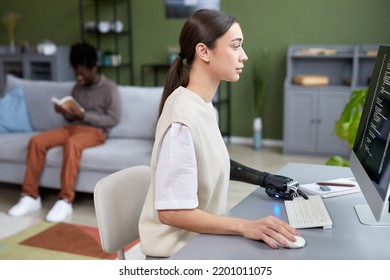 Serious young girl with disability working with codes on computer at her workplace at home with man reading book in background - Powered by Shutterstock