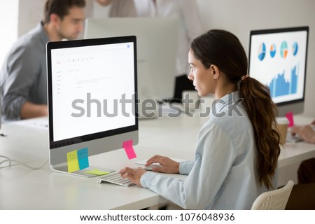Serious young girl intern focused on writing email working on computer, young female office employee or trainee apprentice using pc mail software for corporate clients communication or support