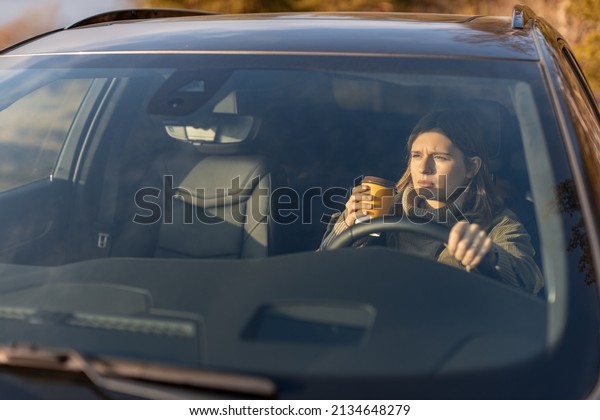 Serious young girl in the morning goes to work\
by car and drinking coffee. View through the windshield. Copy\
space. Transportation\
concept.