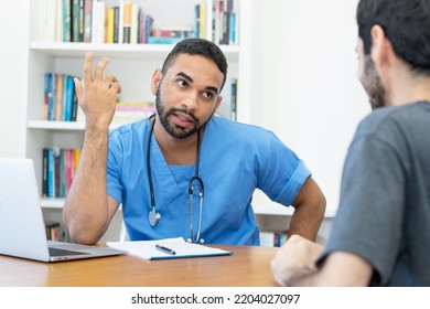 Serious Young Hispanic Doctor Or Nurse Talking With Patient At Office Of Hospital