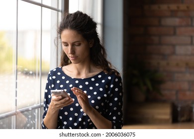 Serious Young Latin Woman Using Mobile Phone At Home, Texting On Virtual Chat, Ordering Service Via Online App, Making Call, Checking Email, Surfing Internet, Social Media, Reading Blog Article