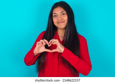 Serious Young Latin Woman Wearing Red Shirt Over Blue Background  Keeps Hands Crossed Stands In Thoughtful Pose Concentrated Somewhere