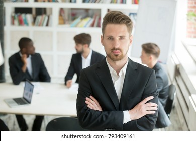 Serious Young Leader In Suit Looking At Camera Standing Arms Crossed On Executive Team Meeting Background, Confident Manager Boss Ceo Co Owner Posing In Front Of Partners Group, Headshot Portrait