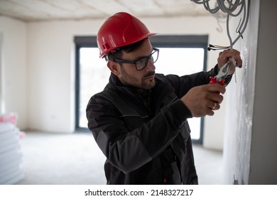 Serious Young Male Electrician With Helmet Holding Cutting Electrical Wires With Pliers.