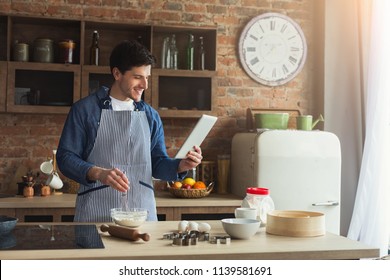 Serious young man baking pie in loft kitchen at home, using digital tablet with recipe, copy space - Powered by Shutterstock