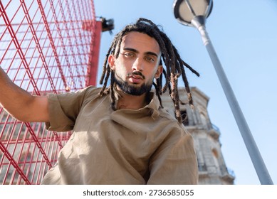 Serious young man with dreadlocks looking at the camera in an urban setting
