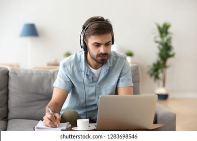 Serious Young Man Looking At Laptop Wearing Headset Learning Foreign Language, Training Knowledge Listening Webinar Making Notes, Online Study, E-coaching, Distance Education, E-learning Concept