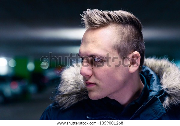 Serious\
young man with a modern haircut standing outdoors in town staring\
intently to the side in a fur trimmed\
jacket
