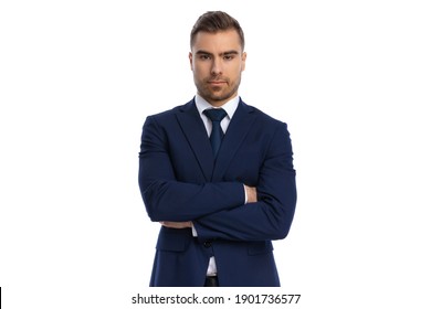 serious young man in navy blue suit folding arms and posing on white background in studio, portrait
