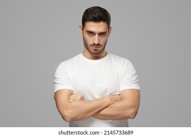 Serious young man portrait. Tough guy standing with crossed arms isolated on grey background