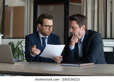 Serious young man supervisor analyse financial report of responsible worker pay attention on mistakes propose correction. Professional insurance agent discuss paper policy terms conditions with client