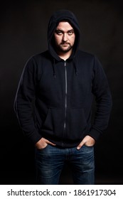 Serious Young Man In A Sweater With A Hood On A Black Background. Vertical. Banditry And Crime.