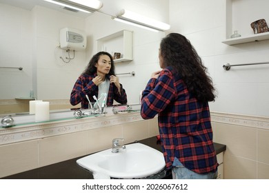 Serious young man taking on plaid shirt in front of bathroom mirror before going out - Powered by Shutterstock