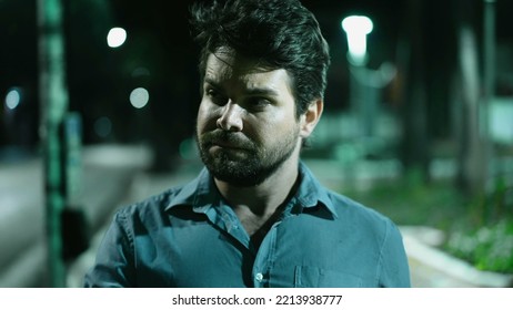 Serious Young Man Walking At Night In Downtown City Street. Thoughtful Pensive Person Walks Forward At Night In Urban Sidewalk