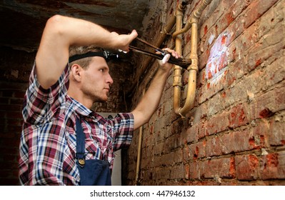 Serious Young Man Wearing Headlight Fixing A Leak With A Pipe Wrench In Basement