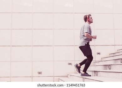 Serious Young Man Wearing Sportswear, Listening To Music And Running Upstairs On City Stairs. Side View.