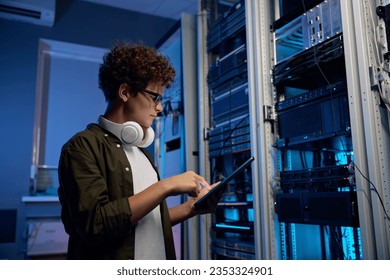 Serious young man working in data center standing at open server rack cabinet