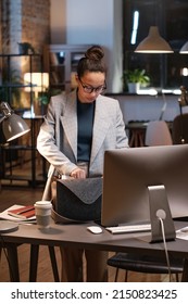 Serious Young Mixed Race Manager In Glasses Standing At Table With Computer And Taking Work Staff While Leaving Office At Night