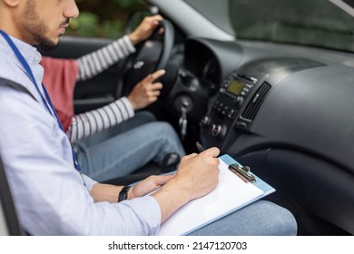 Serious Young Muslim Guy Teacher Taking Driving Test From Woman In Hijab At Steering Wheel Driving Car, Cropped. Mentor Teaches Student To Drive, Driving Class And Good Mark. Education And Study