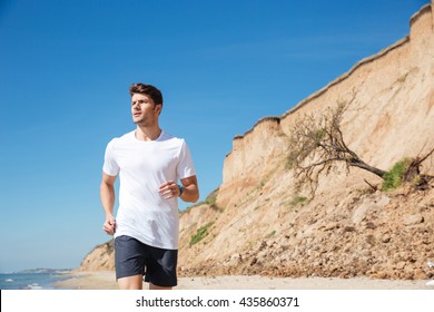 Serious young sportsman in white t-shirt and black shorts running on the beach - Powered by Shutterstock