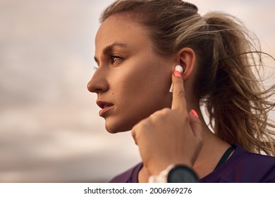Schweres jugendliches sportliches Mädchen, das TWS-Ohrläppchen berührt, während es beim Fitnesstraining im Freien Musik hört