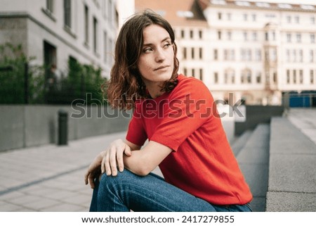 Serious Young Student Sitting on Stone Stairs in the City, Gazing Sideways