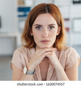 Serious Young Woman With A Deadpan Expression Resting Her Chin On Her Hands As She Stares Intently At The Camera