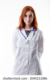 Serious Young Woman Doctor With A Troubled Expression Standing In A White Lab Coat And Stethoscope With Hands Behind Her Back Staring At The Camera