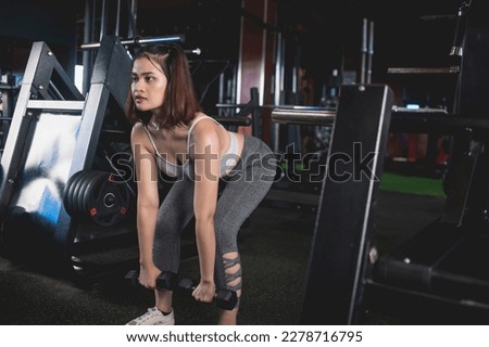 A serious young woman does a set of bent over dumbbell rows. Training and toning back muscles at the gym.
