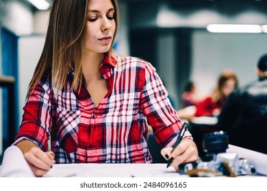 Serious young woman drafting plan for architectural project sitting in coworking space with stationery, pensive female student drawing graphic sketch for homework concentrated on creation design - Powered by Shutterstock