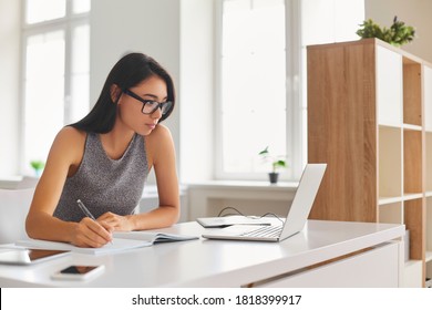 Serious Young Woman Enjoying Self-directed Learning With Online Educational Tools. Bright Student Writing In Notebook And Using Laptop Computer For E-learning Watching Webinar Or Attending E-class